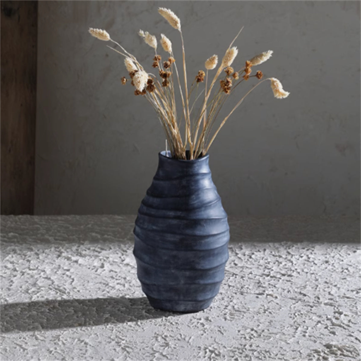 Dark spiral ribbed vase with dried flowers on textured surface