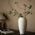Matte white tall vase styled with green branches on a dark table