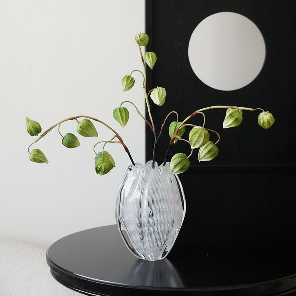 Clear textured glass vase with green botanicals on black table