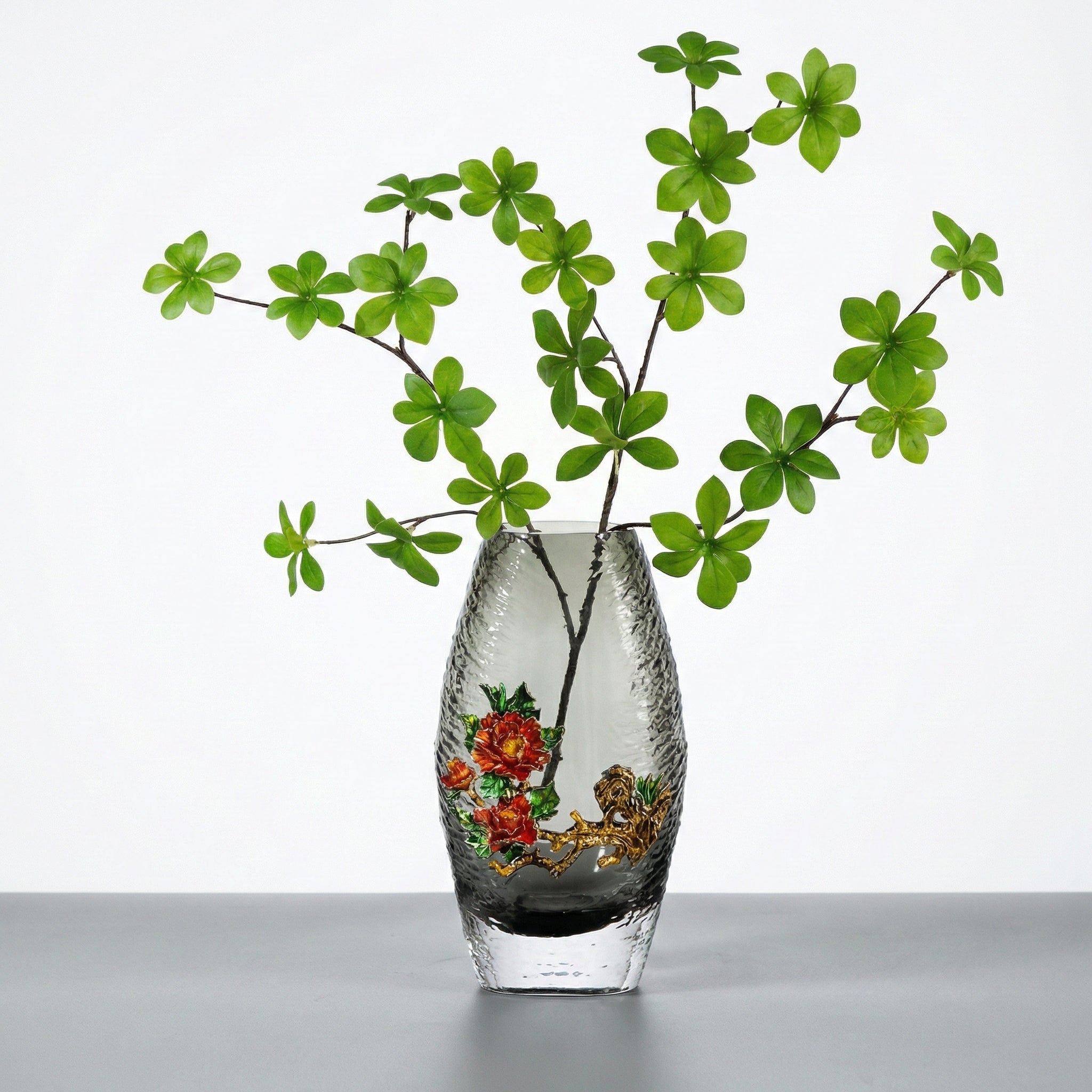 Large grey glass vase with red enamel flowers and green branches holding greenery