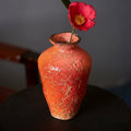 Tall textured orange ceramic vase with single camellia flower
