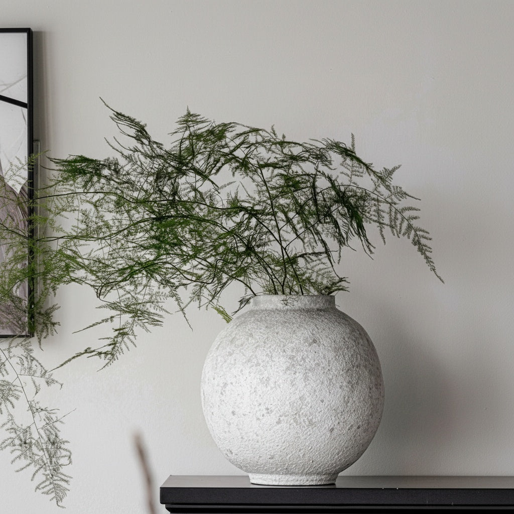 Textured stone finish spherical vase with green foliage on black table