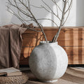 Textured stone finish spherical vase with bare branches in earthy setting
