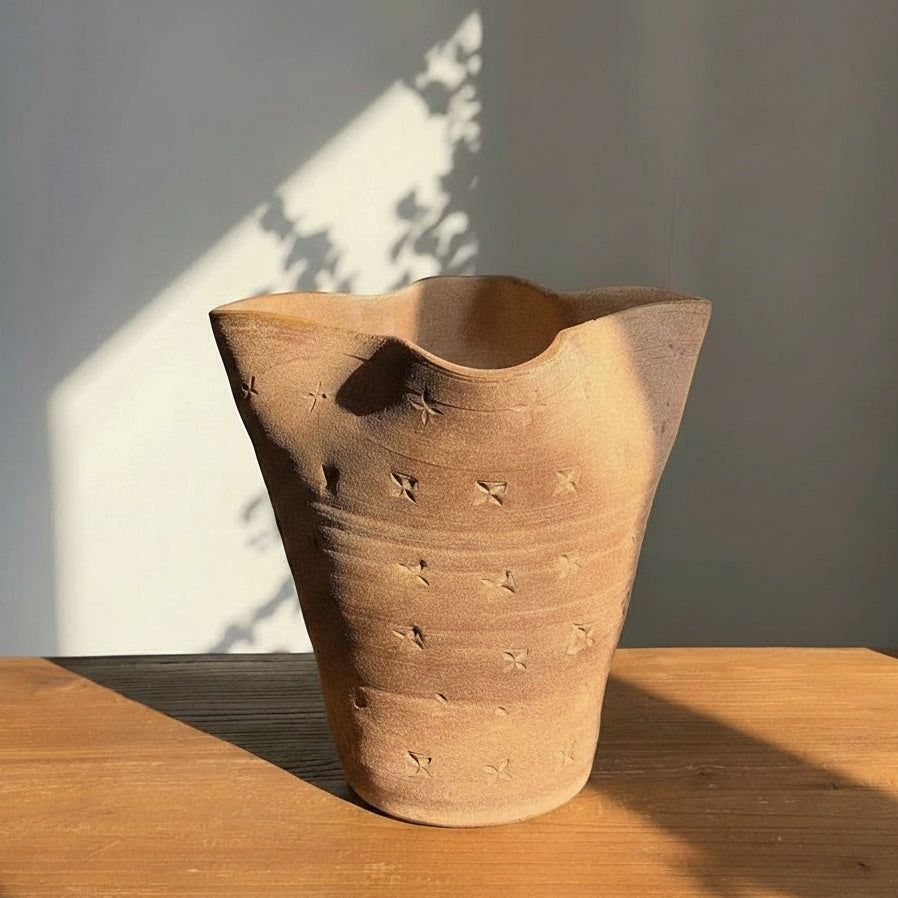 Textured terracotta vase with wavy rim and geometric pattern on wooden table