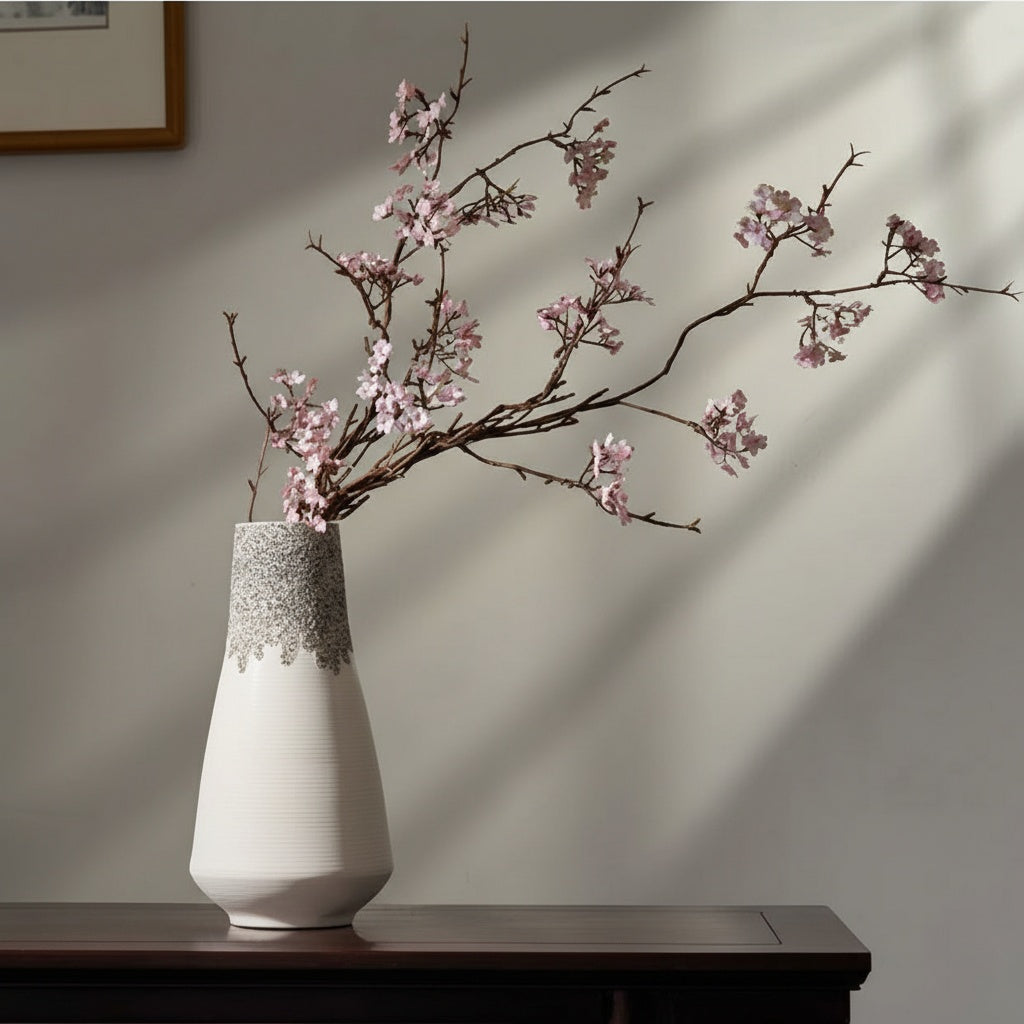 White ceramic vase with ribbed texture and speckled top holding cherry blossoms