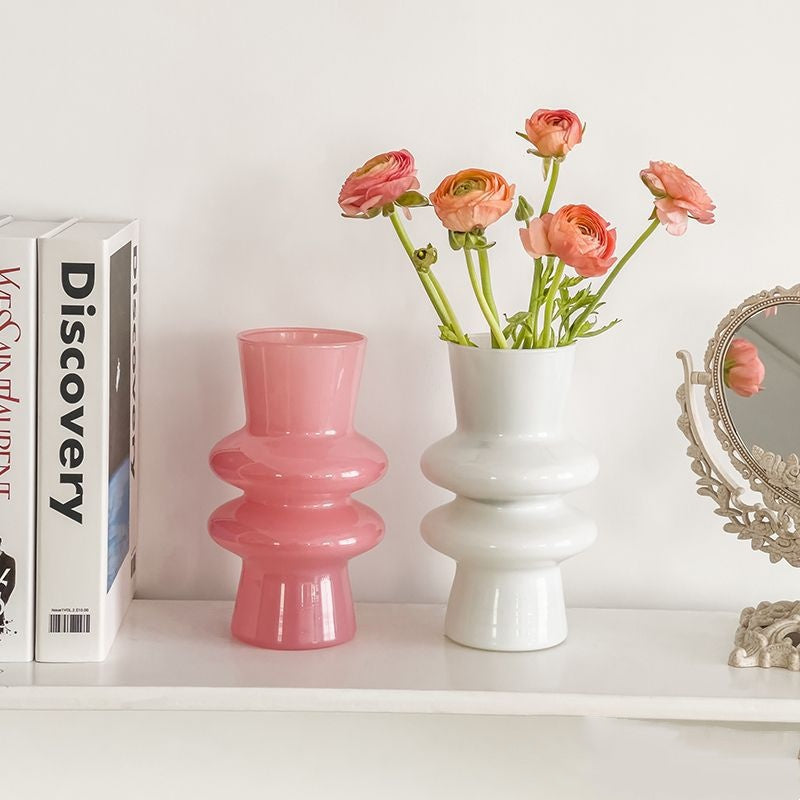 Two tiered glass vases in pink and white holding flowers on a shelf
