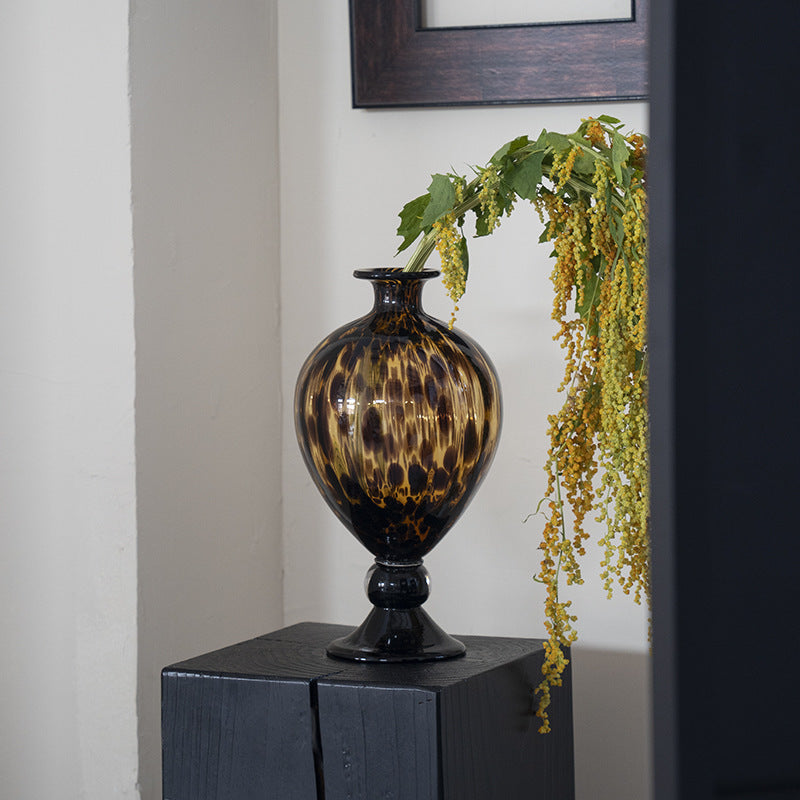 Side view of amber tortoise shell glass urn vase on black plinth