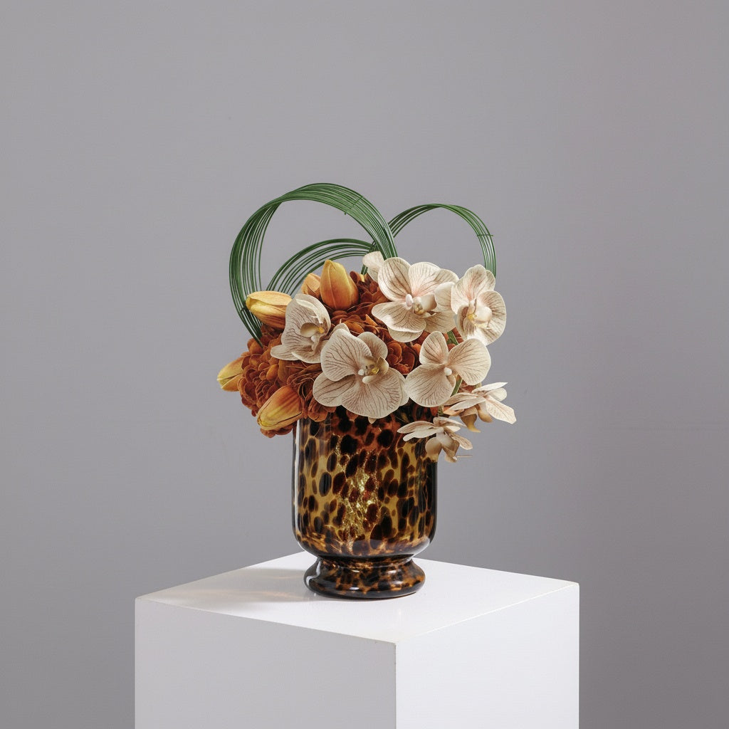Tortoiseshell glass footed vase filled with warm toned floral arrangement