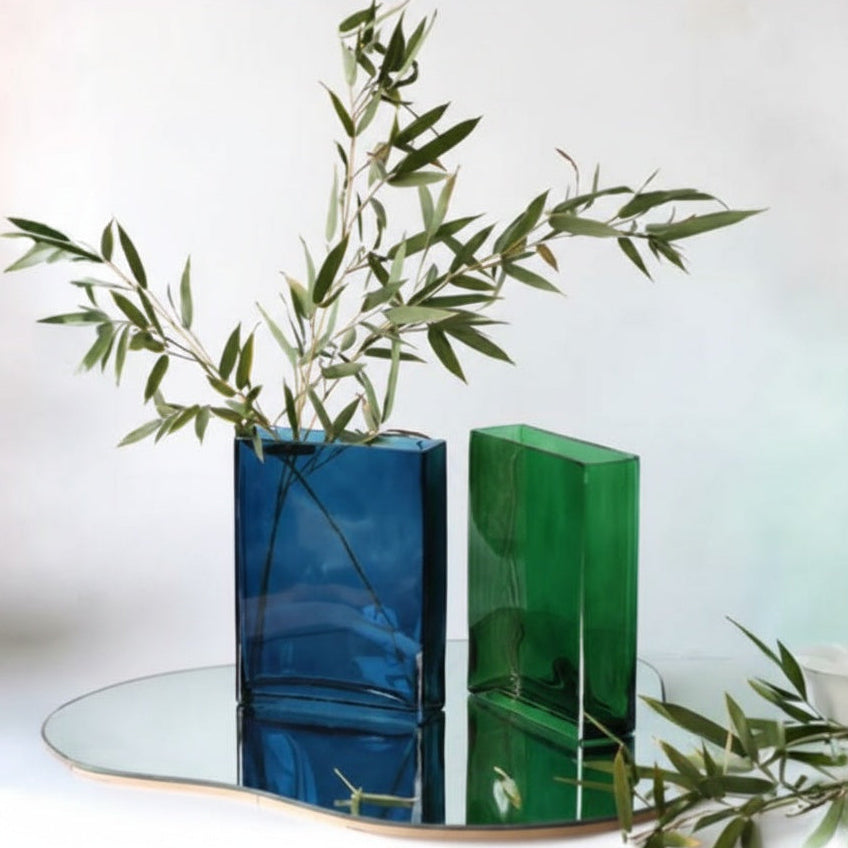 Two curved rectangular glass vases in blue and green on a mirror