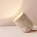 Travertine angled cylinder table lamp illuminated against wall