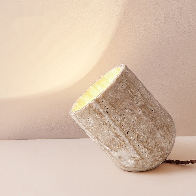 Travertine angled cylinder table lamp illuminated against wall