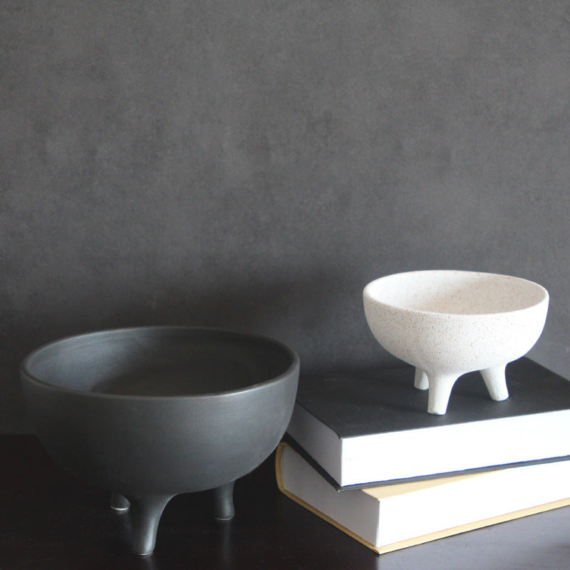 Handcrafted black and speckled cream tripod ceramic bowls styled as modern home decor on a stack of books.