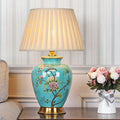 Turquoise ceramic table lamp with floral bird design and pleated shade on side table