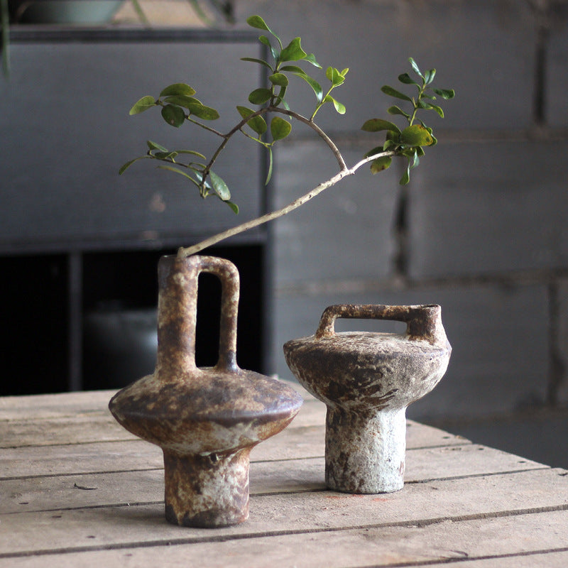 Two rustic ceramic vases with handles on a wooden surface, one containing a branch with leaves.