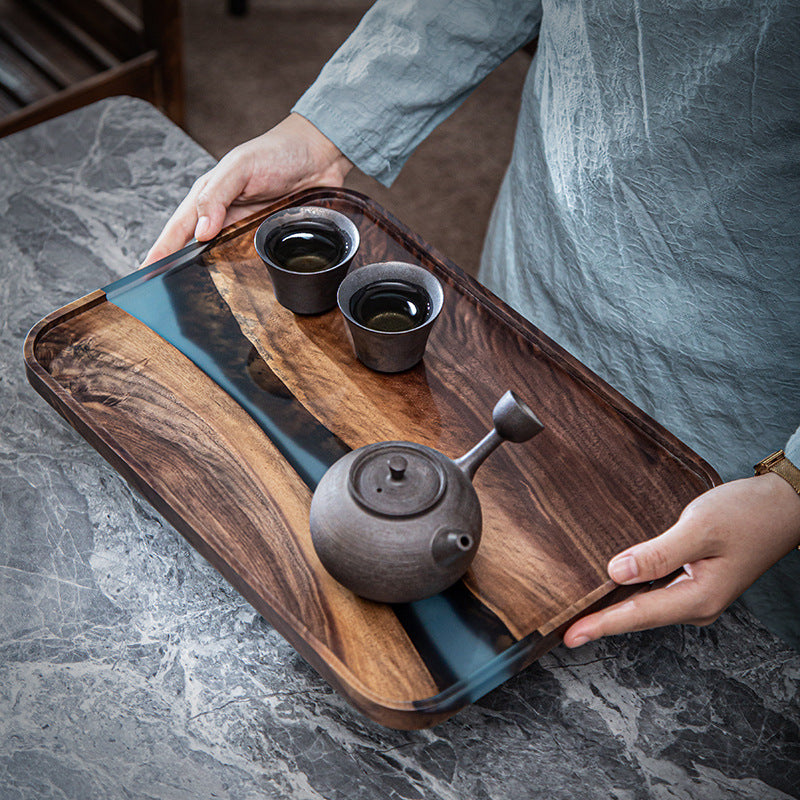 Handcrafted walnut wood serving tray held by a person with tea set and blue resin river detail