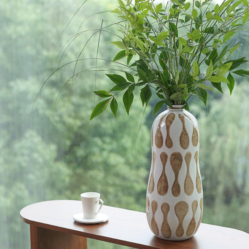 White and brown patterned ceramic vase with greenery on table