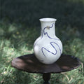 Front view of white ceramic vase with blue abstract art and gold details on dark table