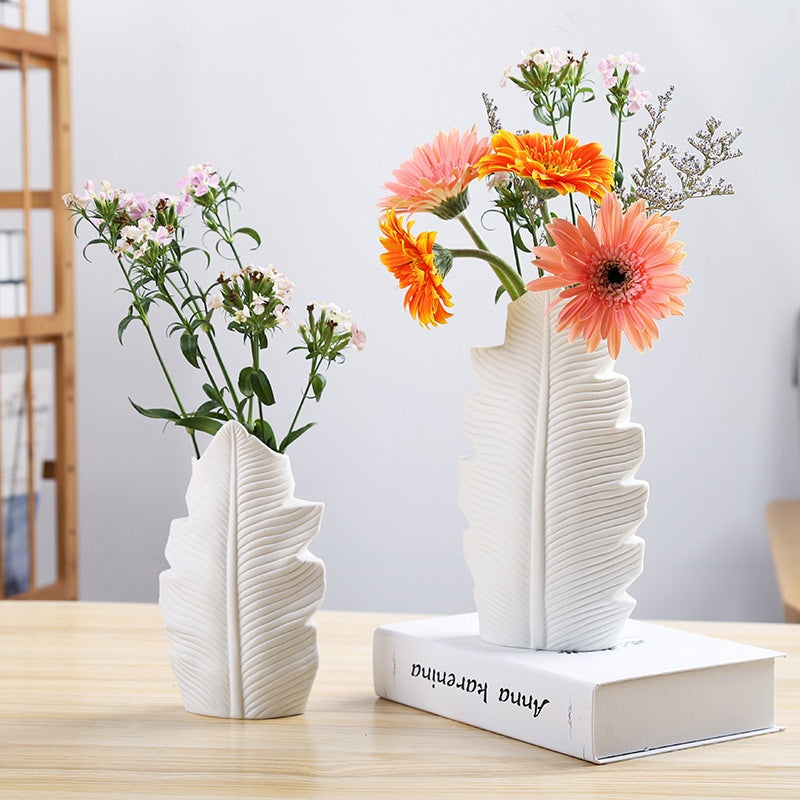 Two ceramic leaf vases with flowers on table