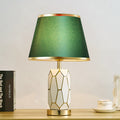 Front view of white ceramic honeycomb lamp with green shade lit up