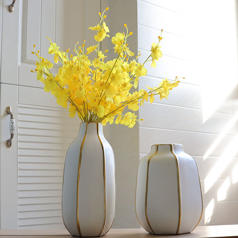 White ceramic vases with gold ribs holding yellow flowers