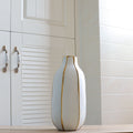 Close up of tall white vase with gold vertical stripes