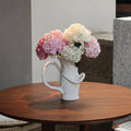 White ceramic sculptural pitcher vase with hydrangea flowers on wooden table