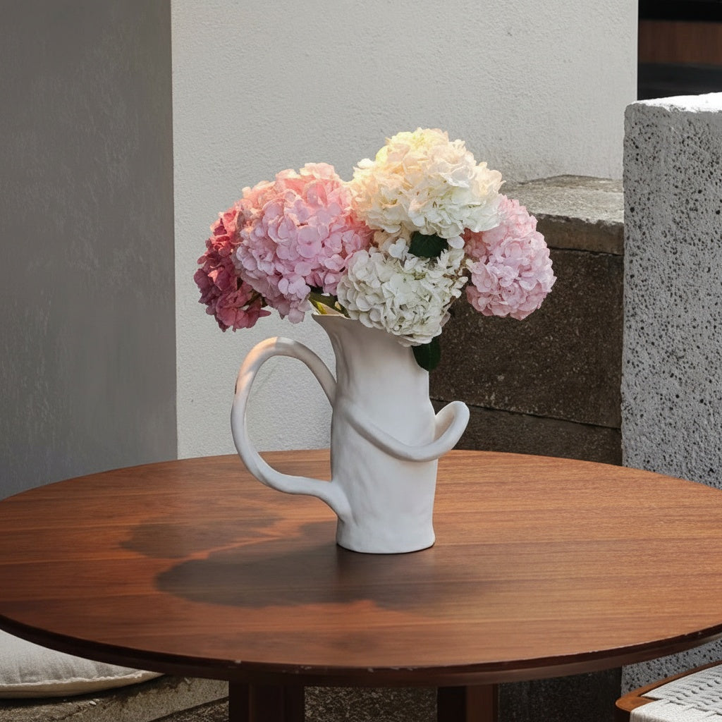 White ceramic sculptural pitcher vase with hydrangea flowers on wooden table