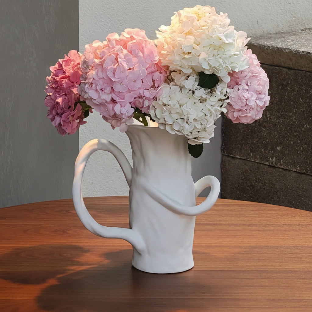 White ceramic pitcher vase holding pink and white flowers in sunlight