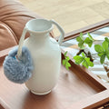 Close up of white ceramic vase with curved handles on a wooden tray
