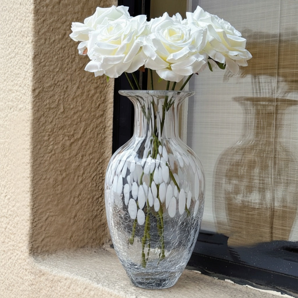 Clear glass vase with white patterns holding white roses on window sill