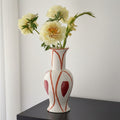 White ceramic vase with red geometric patterns holding yellow flowers