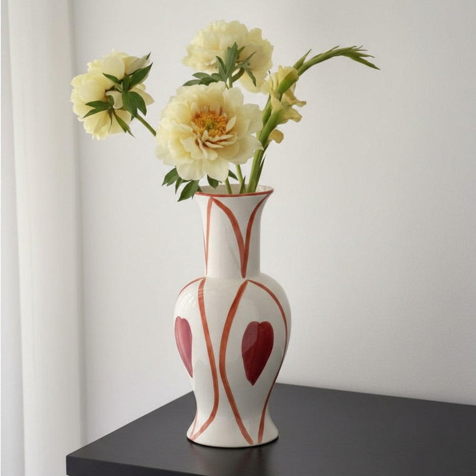 White ceramic vase with red geometric patterns holding yellow flowers