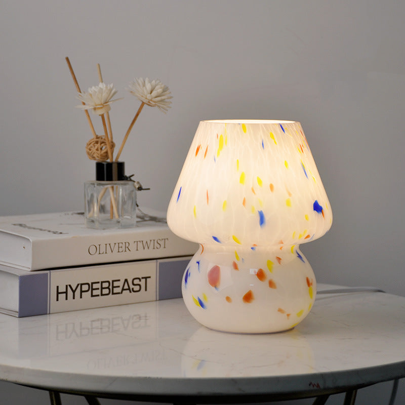 Illuminated white glass mushroom lamp with colorful confetti speckles on a marble side table with books