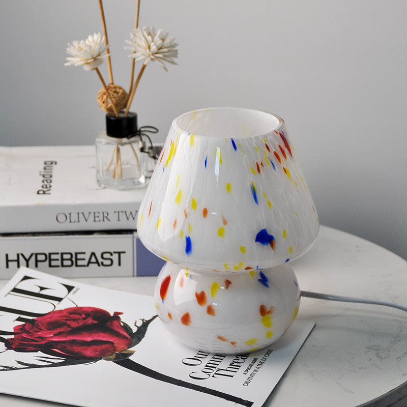 Unlit white glass mushroom lamp with multicolored speckles sitting on a stack of fashion magazines