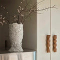 White textured ceramic sculptural vase with branches on a metallic surface