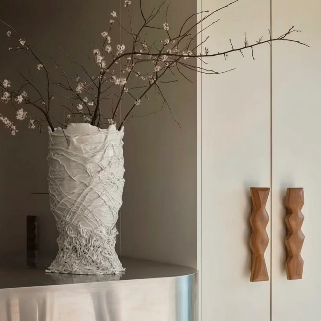 White textured ceramic sculptural vase with branches on a metallic surface